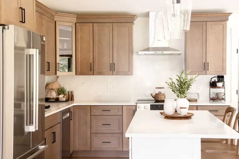 Modern kitchen with light wood cabinetry, white marble countertops and backsplash, stainless steel appliances including refrigerator and range hood, white kitchen island with decorative items, and natural wood accents throughout